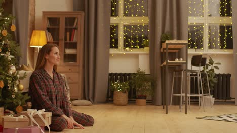 mother waits for her daughter sitting under the christmas tree in the living room while girl runs and hugs her mother