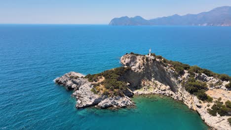 Vuelo-De-Drones-Sobre-La-Isla-En-La-Que-Hay-Un-Faro-Dentro-Del-Mar-Mediterráneo-Contra-El-Fondo-De-Las-Montañas-Y-El-Horizonte