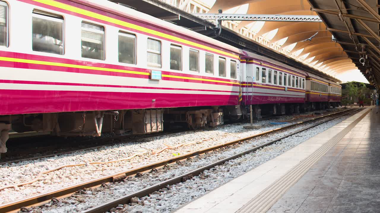 Pengambilan gambar menyamping dari kereta penumpang klasik di peron Bangkok yang tertutup dengan cahaya siang yang lembut