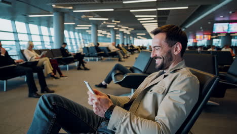man smiling and using phone in a busy airport waiting area