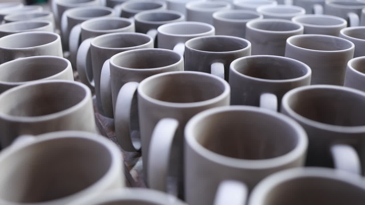 Vista dettagliata dall'alto di file di tazze in ceramica fatte a mano che si asciugano in uno studio di ceramica