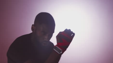 dramatic backlit shot of male boxer in gym wearing wraps on hands training