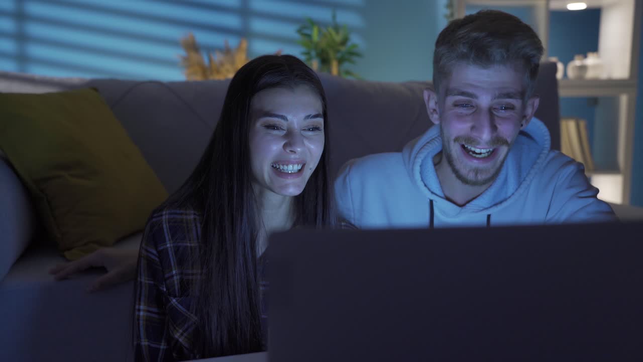 una hermosa joven y un hombre guapo se relajan por la noche mientras ven una película en casa.