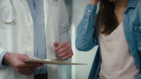 Unrecognizable-caucasian-male-doctor-and-female-patient-discussing-documents-in-corridor-of-health-center