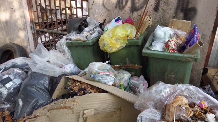 Cumulo di spazzatura e contenitori verdi che straripano di rifiuti di plastica in una struttura abbandonata