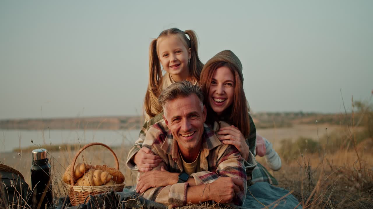 Happy family trio middle aged brunette man his wife and little daughter relaxing having fun and posing during their vacation on a picnic outside the city in summer