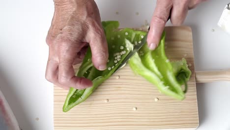 caucasian person with old hands cut green pepper on a wooden board, fish on one side of the plane