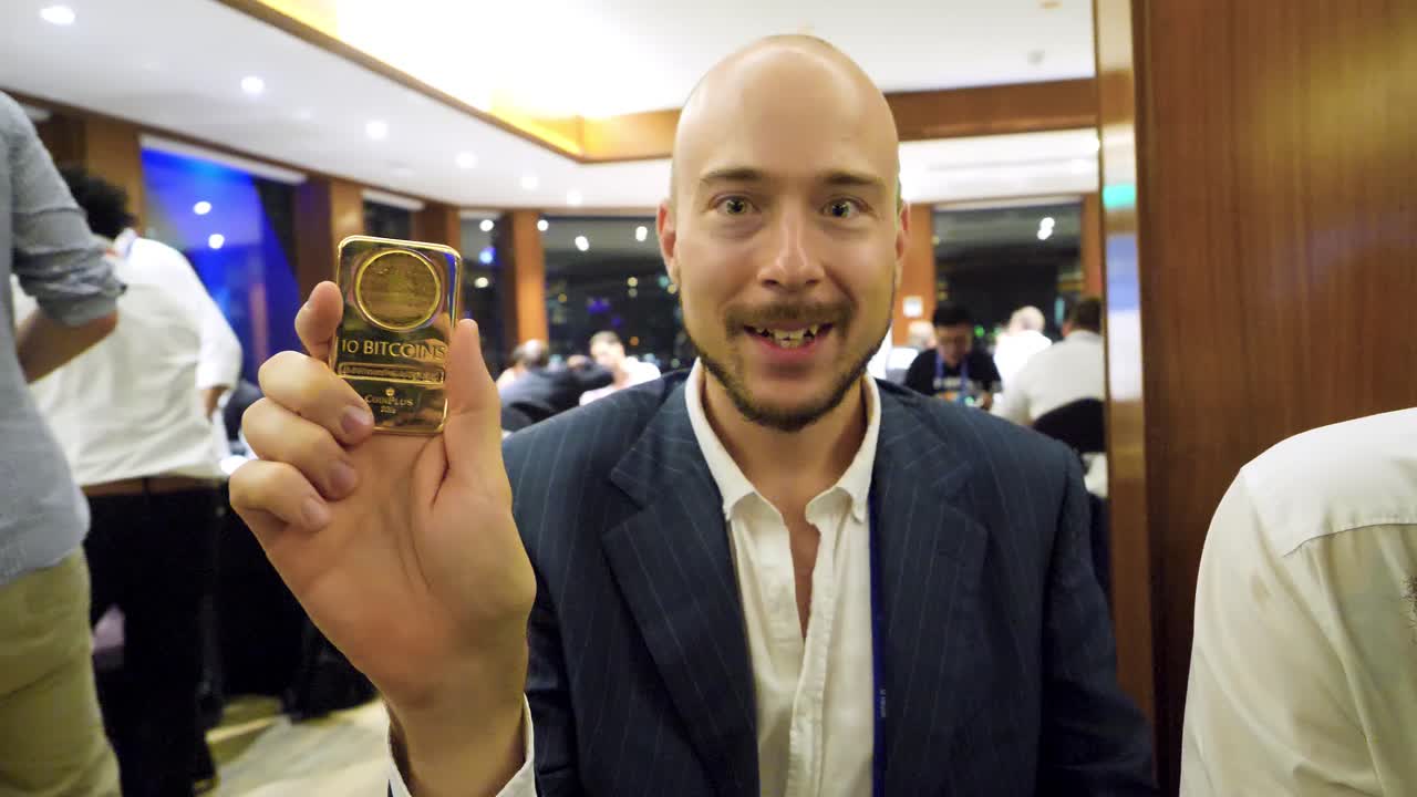 hombre sosteniendo una moneda de oro bitcoin en un evento de negocios