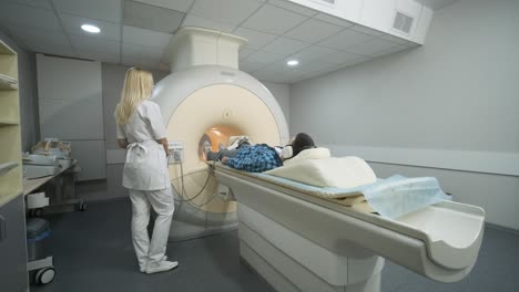 woman doctor makes knee-joint mri scanning. young man patient on automatic table enters into a closed-type mri machine using noise isolation headphones. modern equipment, coil on the patient's knee