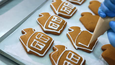 Hand in gloves decorates gingerbread houses with white icing. Close up. Pastry manufacturing at confectionery factory.