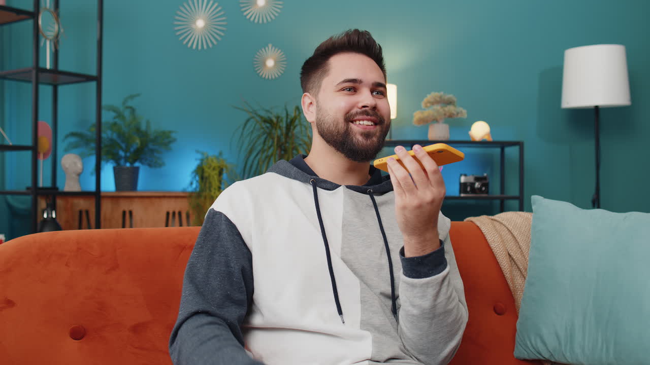 Happy excited young man making phone conversation talking with friend sitting call on couch at home