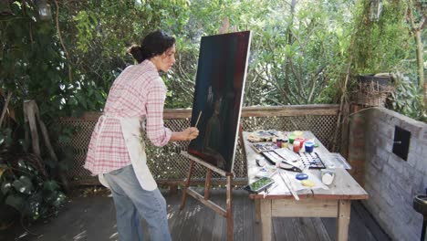 Artista-Birracial-Pintando-Sobre-Lienzo-En-Un-Jardín-Soleado,-Cámara-Lenta