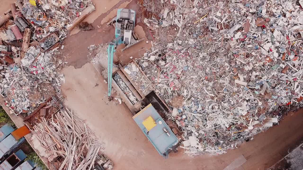 Top down aerial view onto a junk yard trash metal site where an bulldozer is separting the good from the bad bits filmed by drone