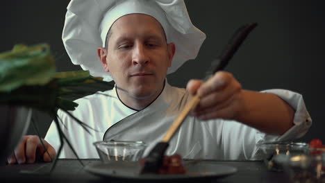 retrato de un chef masculino usando un pincel de silicona con salsa en un plato de carne gourmet. primer plano.