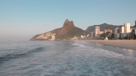 vista aérea baja sobre las olas que entran en la playa de la ciudad costera de río de janeiro durante la hora dorada de la madrugada