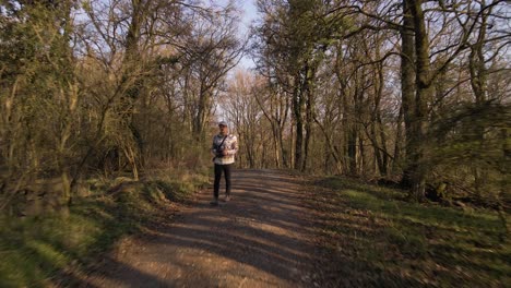 Fly-By-Shot-Of-A-Young-Man-Walking-Along-A-Remote-Trail-Enclosed-By-Bare-Trees