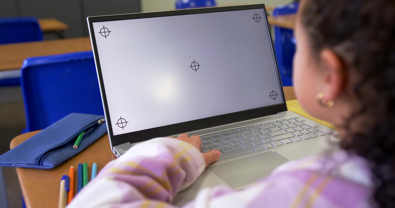Adolescente afroamericano che usa il trackpad del portatile, reagendo a indicatori sullo schermo al banco di scuola, con spazio per il testo