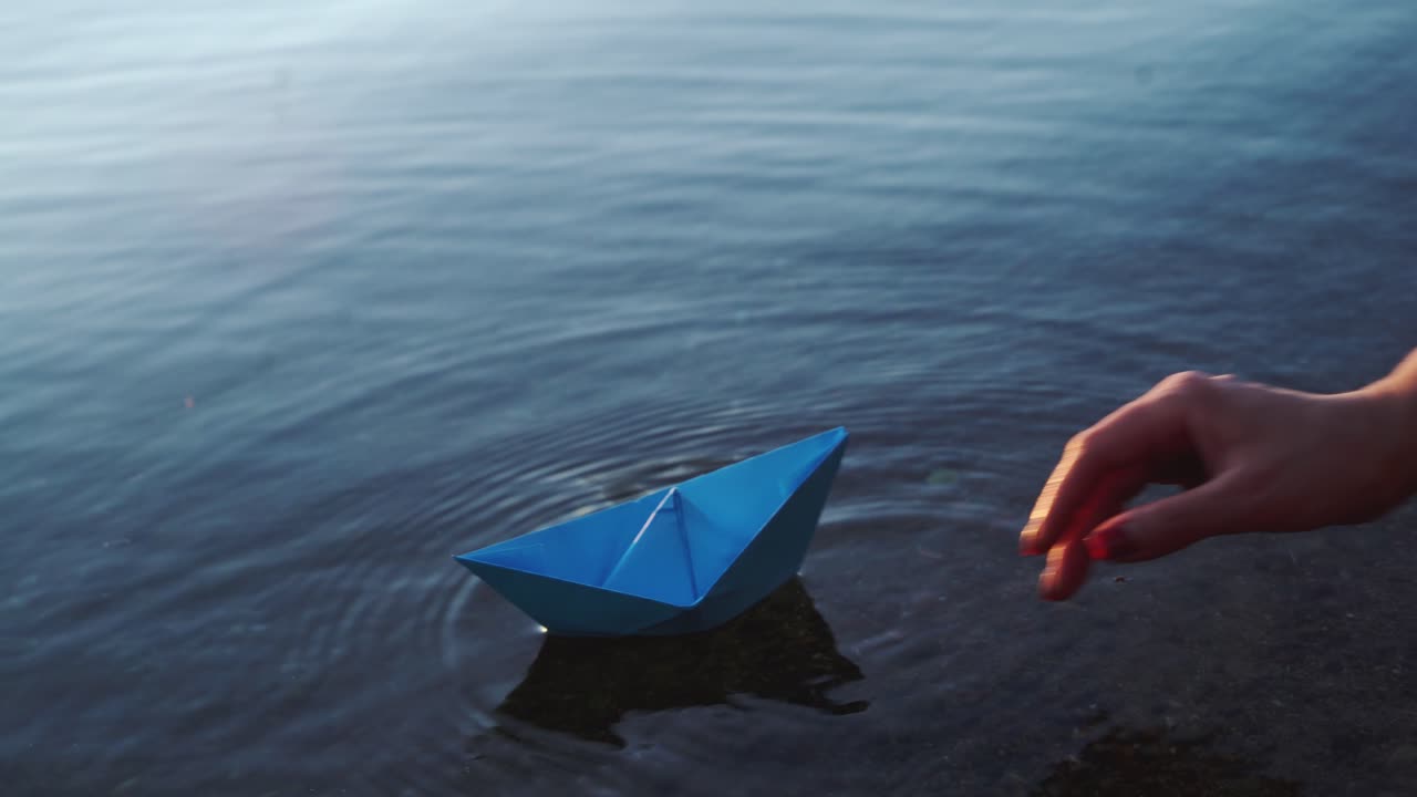 Paper ship in children hand. Blue paper ship. Beautiful sunset