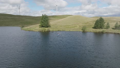 Luftaufnahme-Einer-Jungen-Frau-Auf-Einem-Stand-Up-Paddleboard-Mit-Sich-Drehenden-Windmühlen-Im-Hintergrund