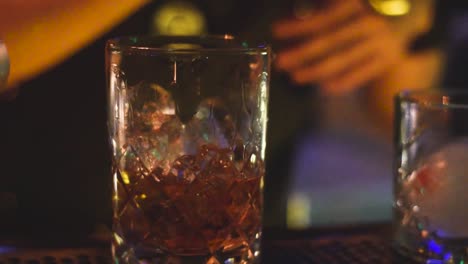 bartender stirring glass of whiskey in dim nightclub