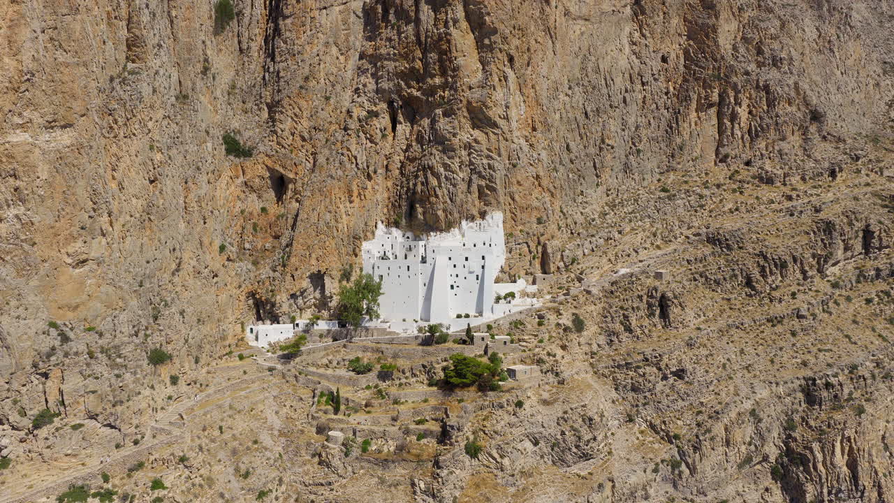 Hozoviotissa Monastery with blue sea and rugged cliffs, Amorgos Island, Greece, drone pulls away pullback establish