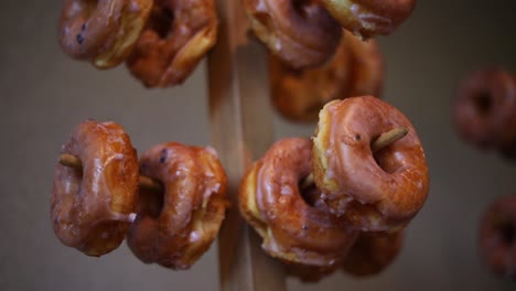 Langsamer-Schwenk-über-Dutzende-Von-Glasierten-Donuts,-Die-An-Mehreren-Donut-Racks-Hängen