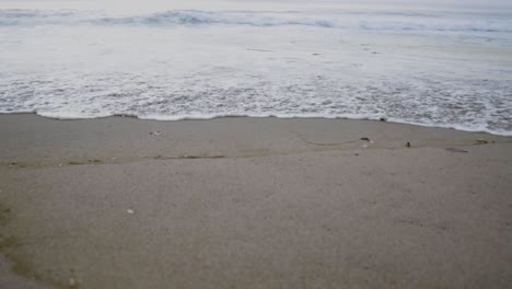 Slow-motion-waves-gently-roll-on-the-Pacific-Ocean-on-an-overcast-day,-capturing-the-rhythmic-and-calming-motion-of-the-water-against-the-backdrop-of-a-grey,-cloudy-sky