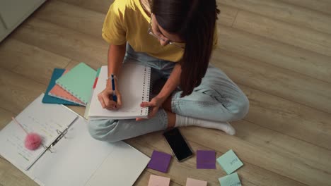 caucasian teenage girl sitting on floor and learning from flash cards and notebook