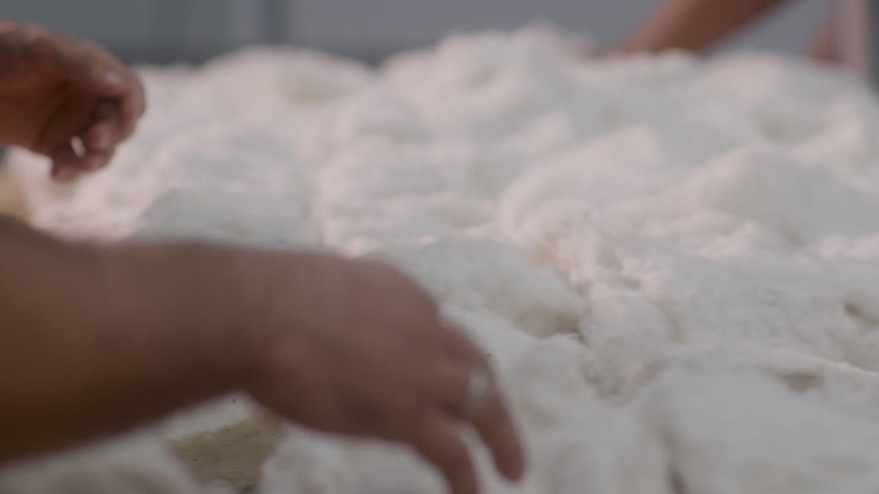 Vista ravvicinata di un operaio che ispeziona materiale di cotone grezzo in una fabbrica tessile.