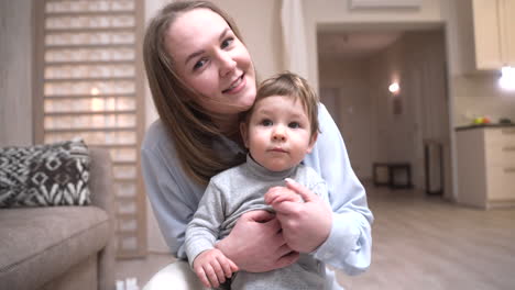 mother holds her baby who is standing on the floor in the living room at home 1