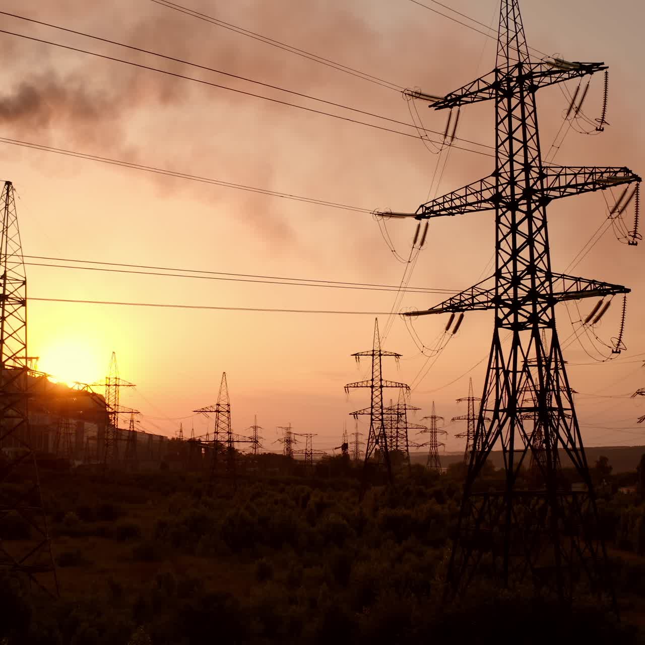 Electric towers near factory chimney with dark smoke. Transmission lines on background of harmful fumes from industry releasing from pipes at sunset. Environment pollution
