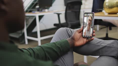 hombre de negocios afroamericano usando un teléfono inteligente para una videollamada con un colega de negocios caucásico