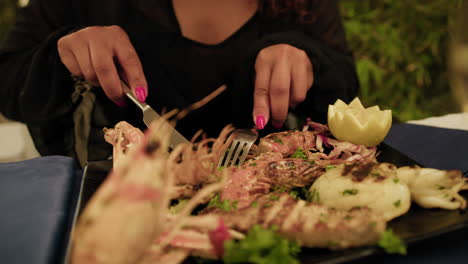 woman eating a mixture of grilled fish during a gourmet restaurant dinner