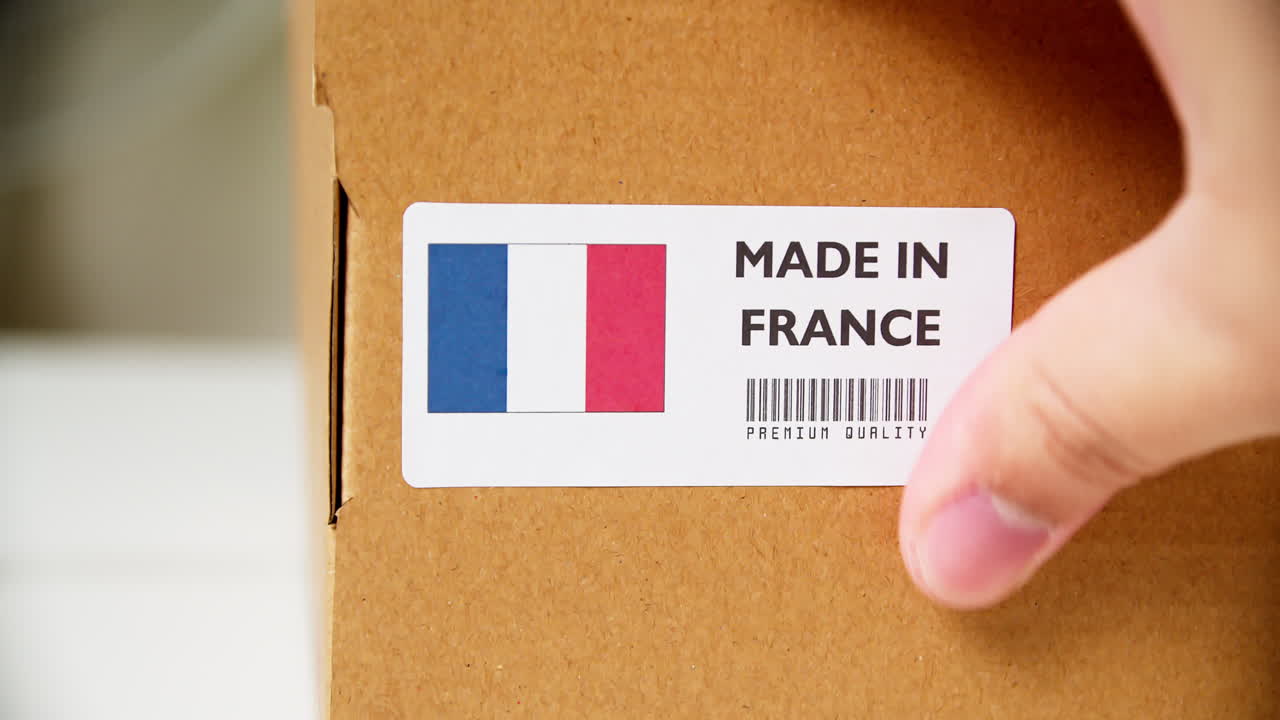 Mani che applicano l'etichetta con bandiera MADE IN FRANCE su una scatola di cartone da spedizione con prodotti.