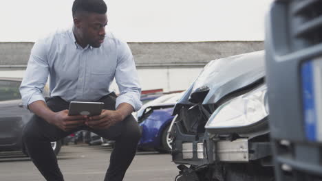 insurance loss adjuster with digital tablet inspecting damage to car from motor accident