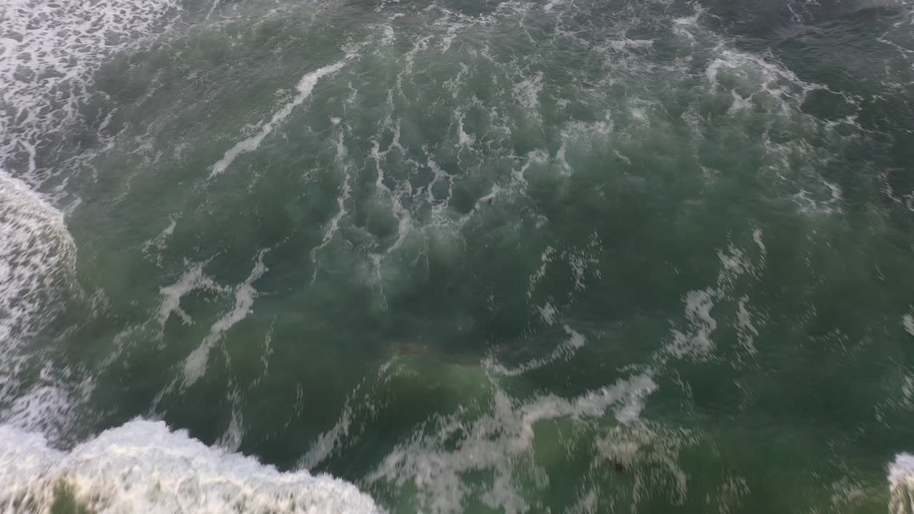 Discover the beauty of the rugged cliffs in the background, as the drone shot slowly pans down to reveal the mesmerizing crashing waves below
