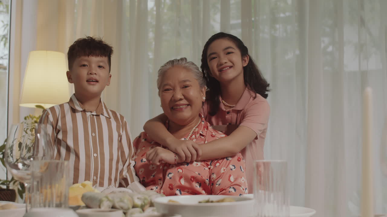 Cheerful Grandmother and Grandkids Smiling at Camera during Dinner