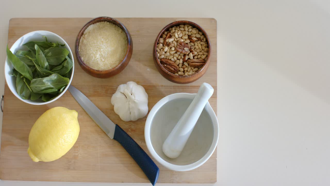 Camera is zooming to center cutting board with basil, cheese, garlic on counter, copy space