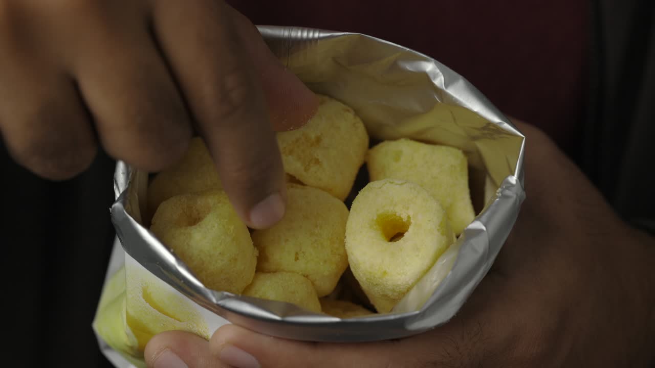 cerca de un joven comiendo anillos de maíz crujientes bocadillos salados en una bolsa de papel. comida rápida o comida chatarra bocadillos concepto no saludable.