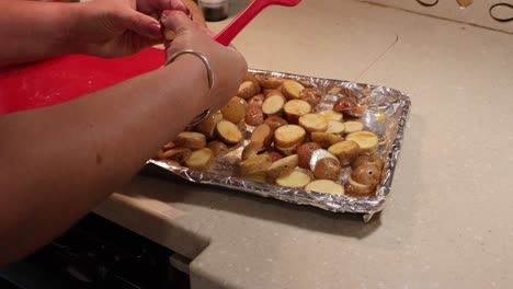 close up of woman breaking up and laying flat sliced baby potatoes on a pan ready for roasting in an rv kitchen