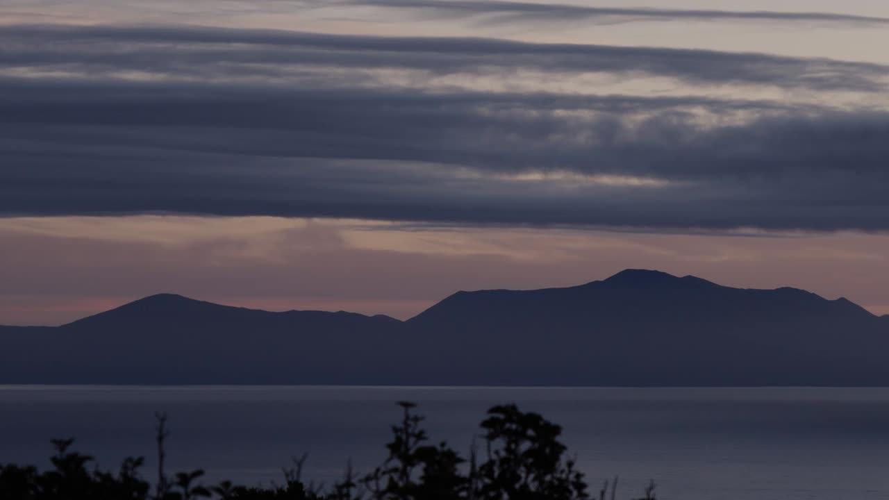 해가 지는 동안 바다와 먼 산과 함께 아름다운 뉴질랜드 풍경