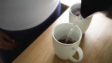 mano vertiendo agua en mis tazas para café y té para pareja en una mesa de madera por la mañana