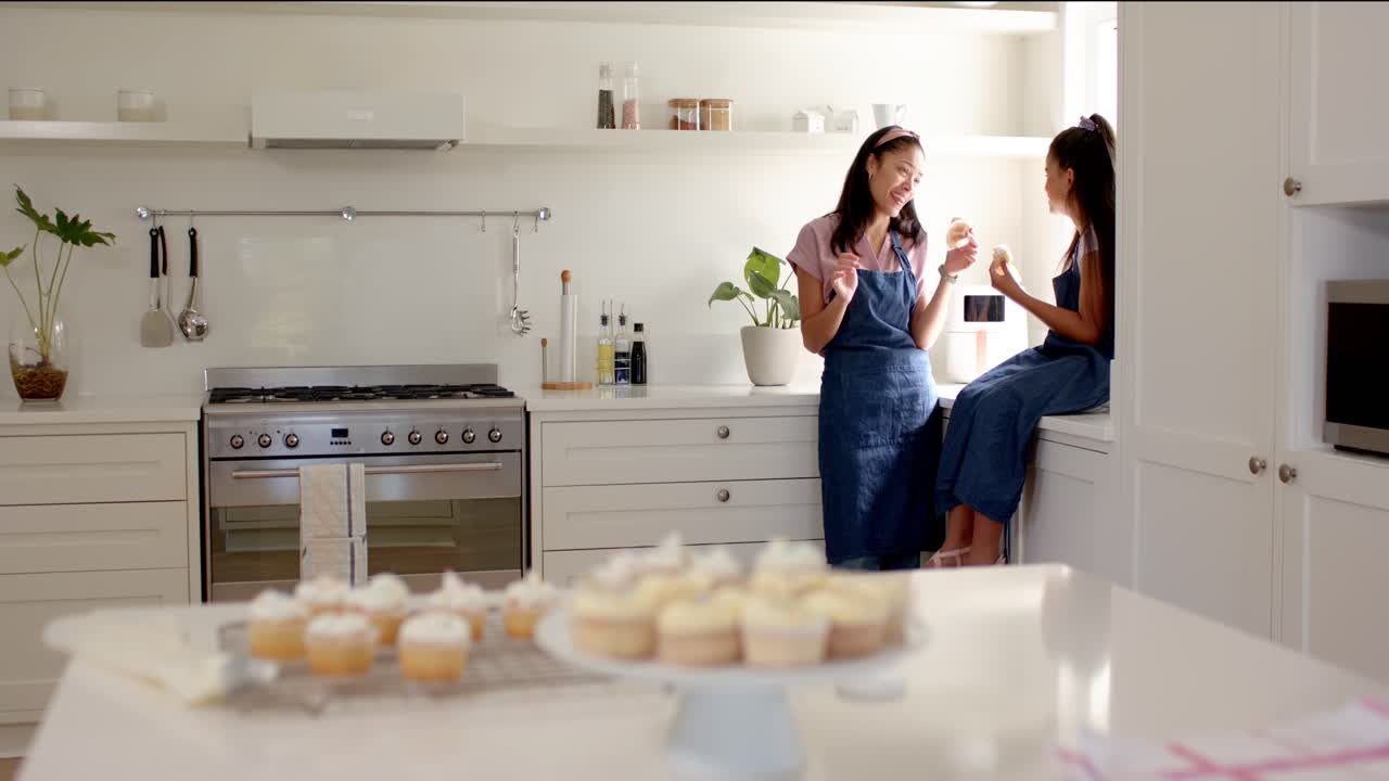 Cupcake freschi, madre e figlia adolescente afroamericane in grembiule assaggiano in cucina, spazio per il testo.