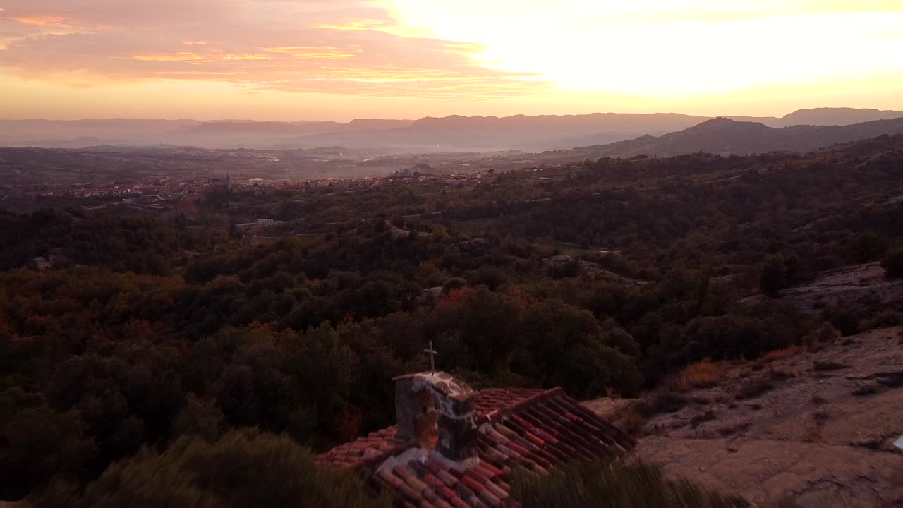 vista aérea de una capilla de montaña mediterránea detrás de un árbol al atardecer