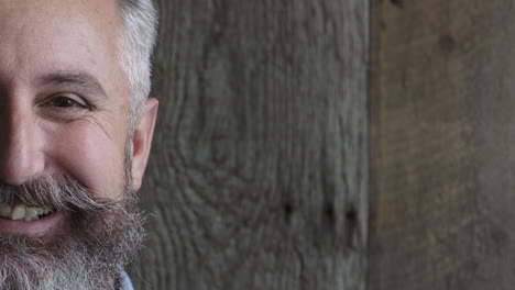 half face portrait of mature bearded man looking at camera smiling cheerful enjoying success satisfaction caucasian male on wooden background copy space close up