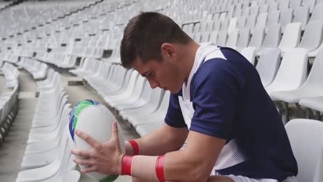 Male-rugby-player-sitting-with-rugby-ball-in-stadium-4k