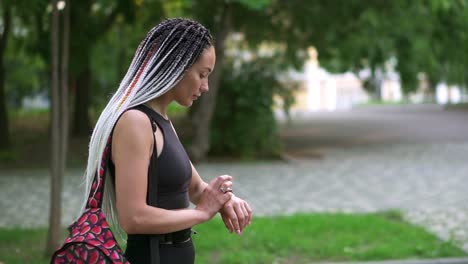 mujer joven concentrada caminando al trabajo o entrenando en el parque, usa su reloj inteligente, tocando en él. estado de ánimo positivo