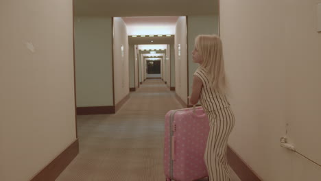 young girl with pink suitcase in hotel corridor