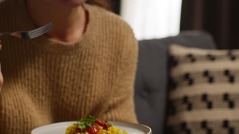 mujer en casa sentada en el sofá comiendo una comida saludable vegetariana o vegana de pasta de orzo con tomates asados con un vaso de vino viendo el programa en la computadora portátil