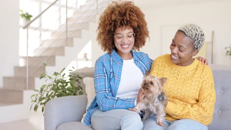 Happy-diverse-female-lesbian-couple-embracing-and-petting-dog-in-living-room-in-slow-motion